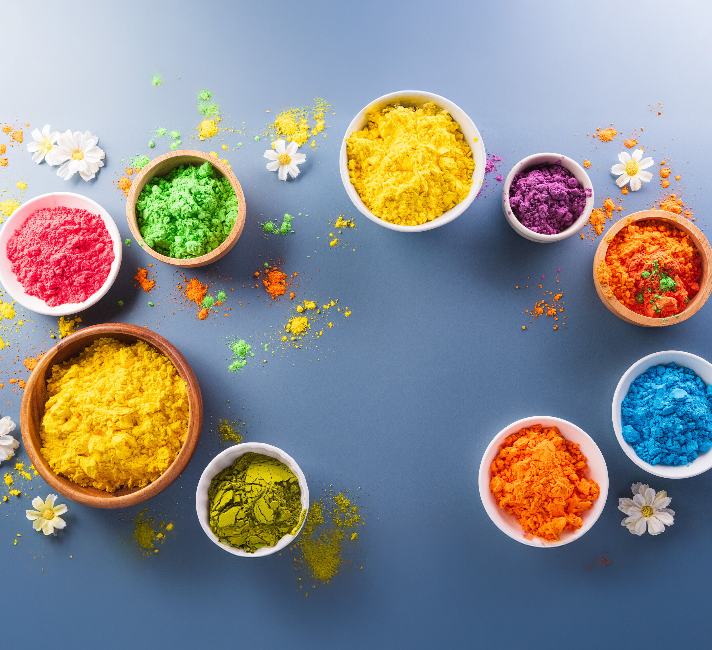 Man playfully pours colorful Holi powder onto a woman&rsquo;s hair as she laughs and wipes color from her face, both dressed in festive outfits and covered in bright hues